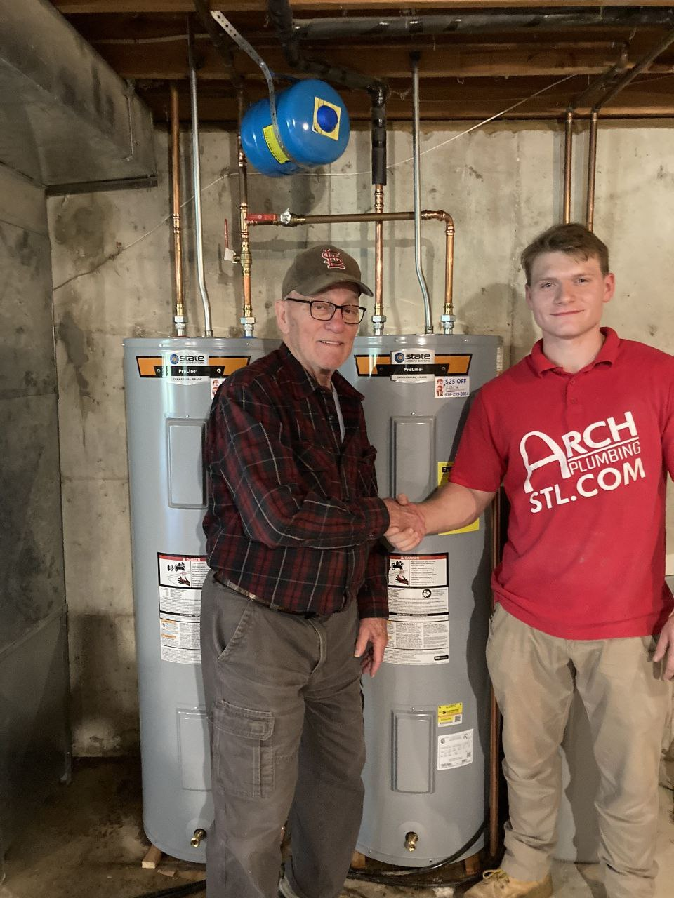 Arch Plumbing technician shaking hands with a happy customer in front of newly installed water heaters